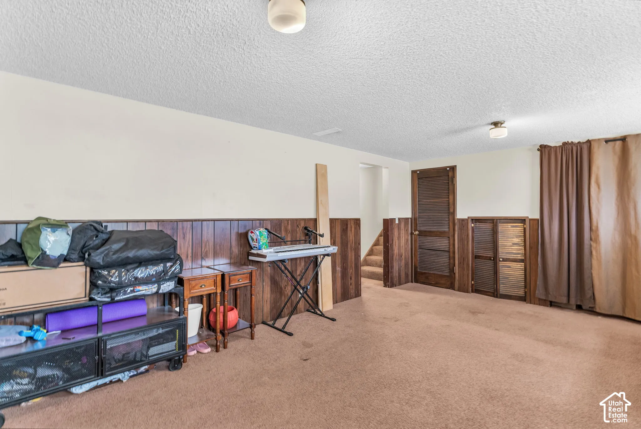 Spacious room featuring wood paneling, carpeted flooring, and a ceiling-mounted light fixture