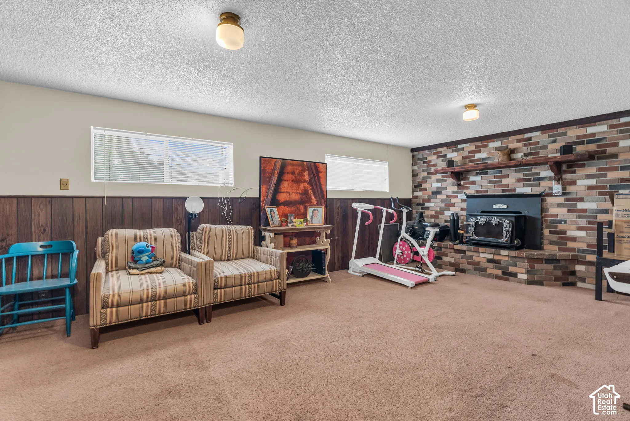Recreation room featuring a brick accent wall with a built-in fireplace, wood paneling, and a neutral carpeted floor