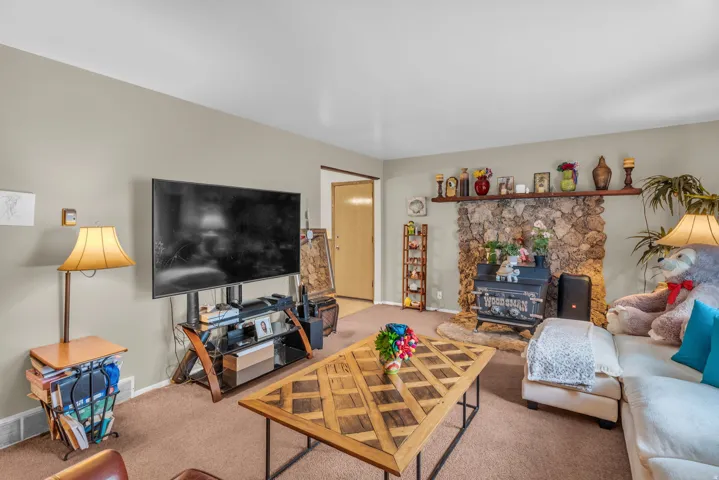 Living area featuring a stone fireplace with a wood-burning insert, a wood mantel, and neutral wall paint