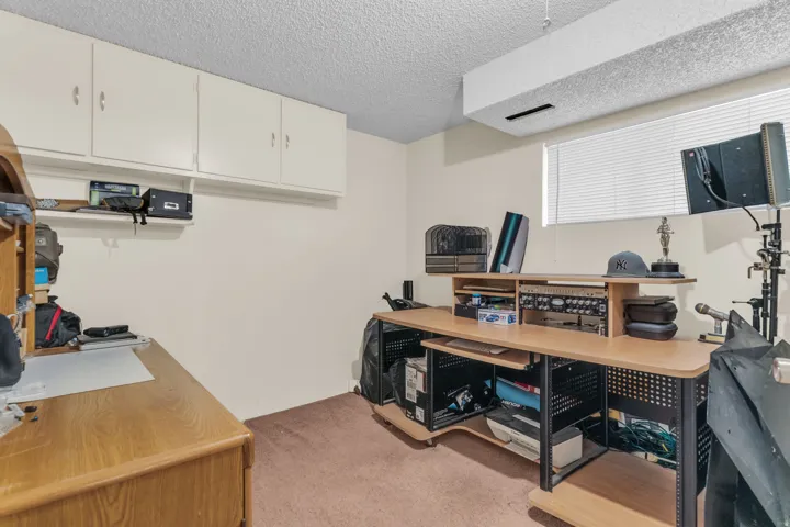 Room featuring a window with blinds, overhead cabinetry, and textured ceiling