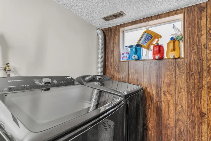 Dedicated laundry area featuring wood-paneling accents, a window, and a textured ceiling