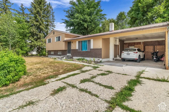 Split-level residence featuring a brick and siding exterior, an integrated carport, mature trees, and a concrete driveway