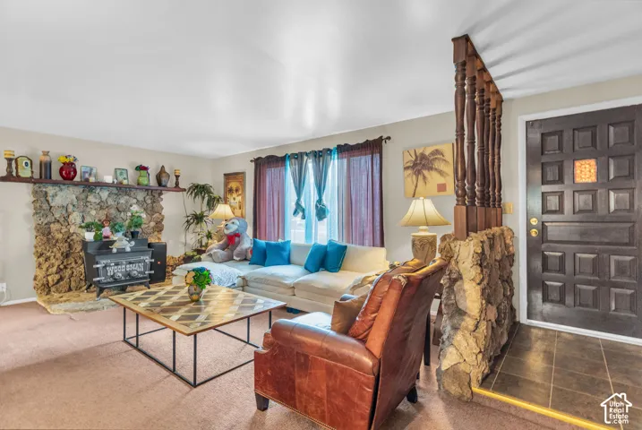 Living room featuring a large stone fireplace with a wood stove, a paneled front door with a decorative glass insert, and a stone accent wall with a wooden railing