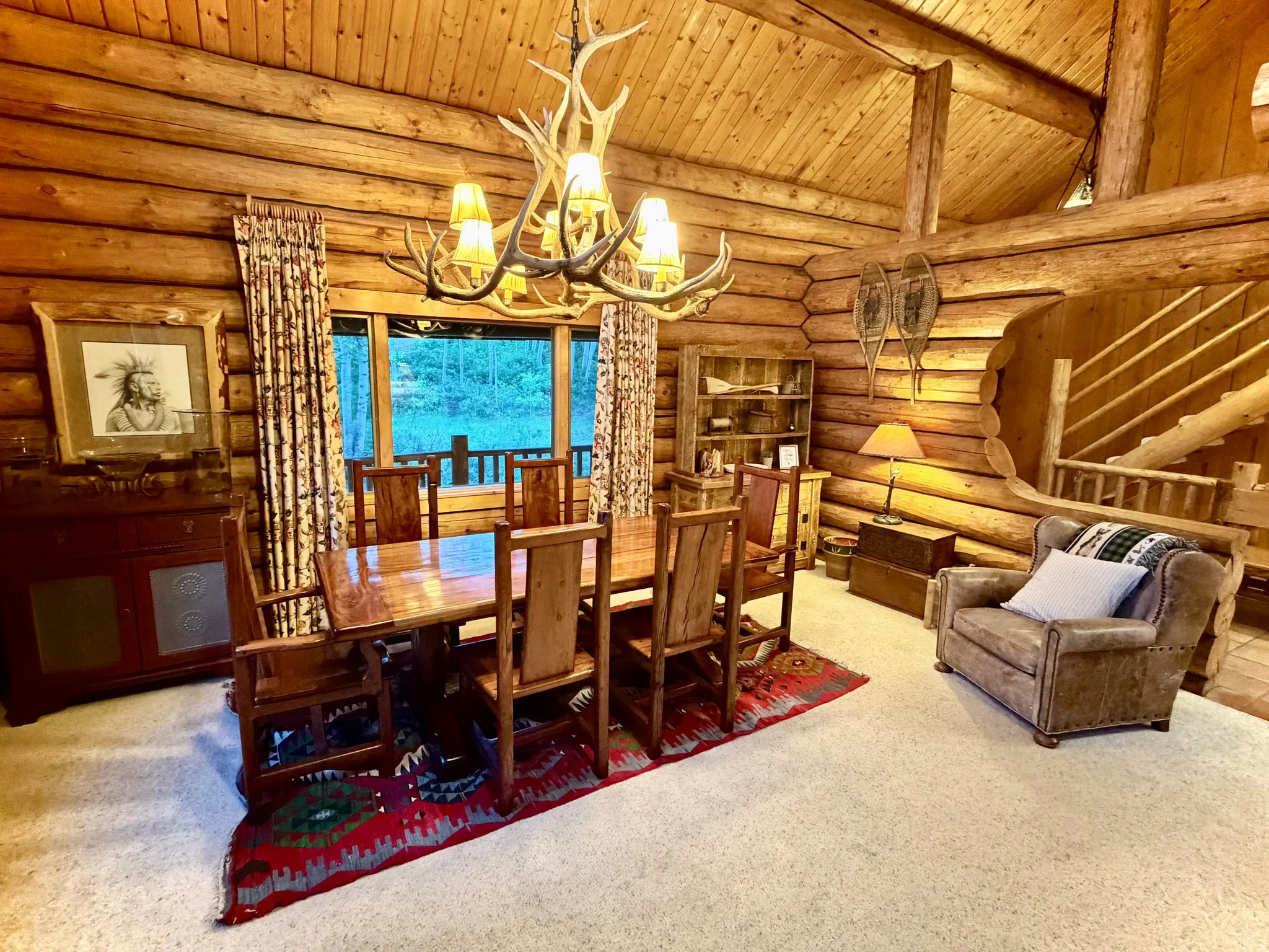 Log cabin interior featuring exposed wood beams, a vaulted ceiling, and a prominent antler chandelier