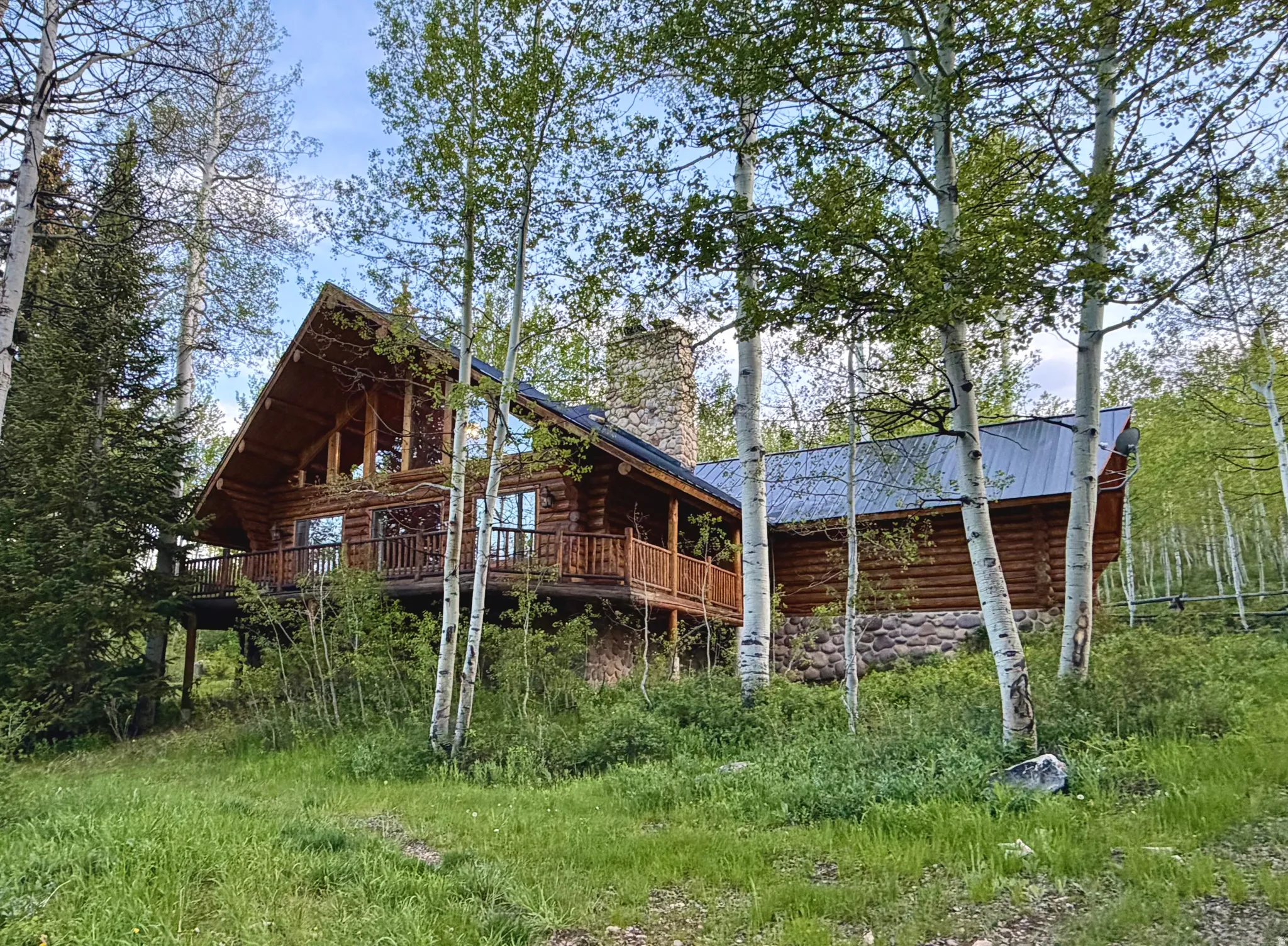 Log home featuring a prominent A-frame structure with expansive windows, a full-length balcony with wood railing, natural log siding, a stone foundation, and a metal roof