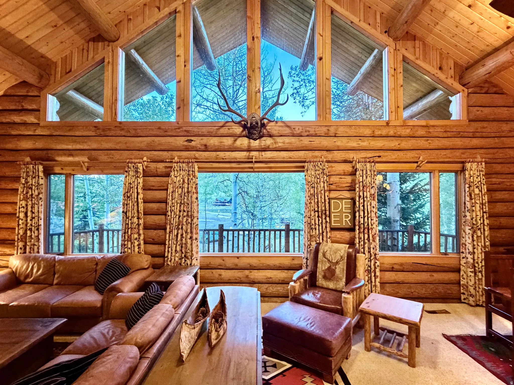 Great room featuring floor-to-ceiling windows, exposed log wall construction, natural wood vaulted ceilings, and a wood-finish balcony railing