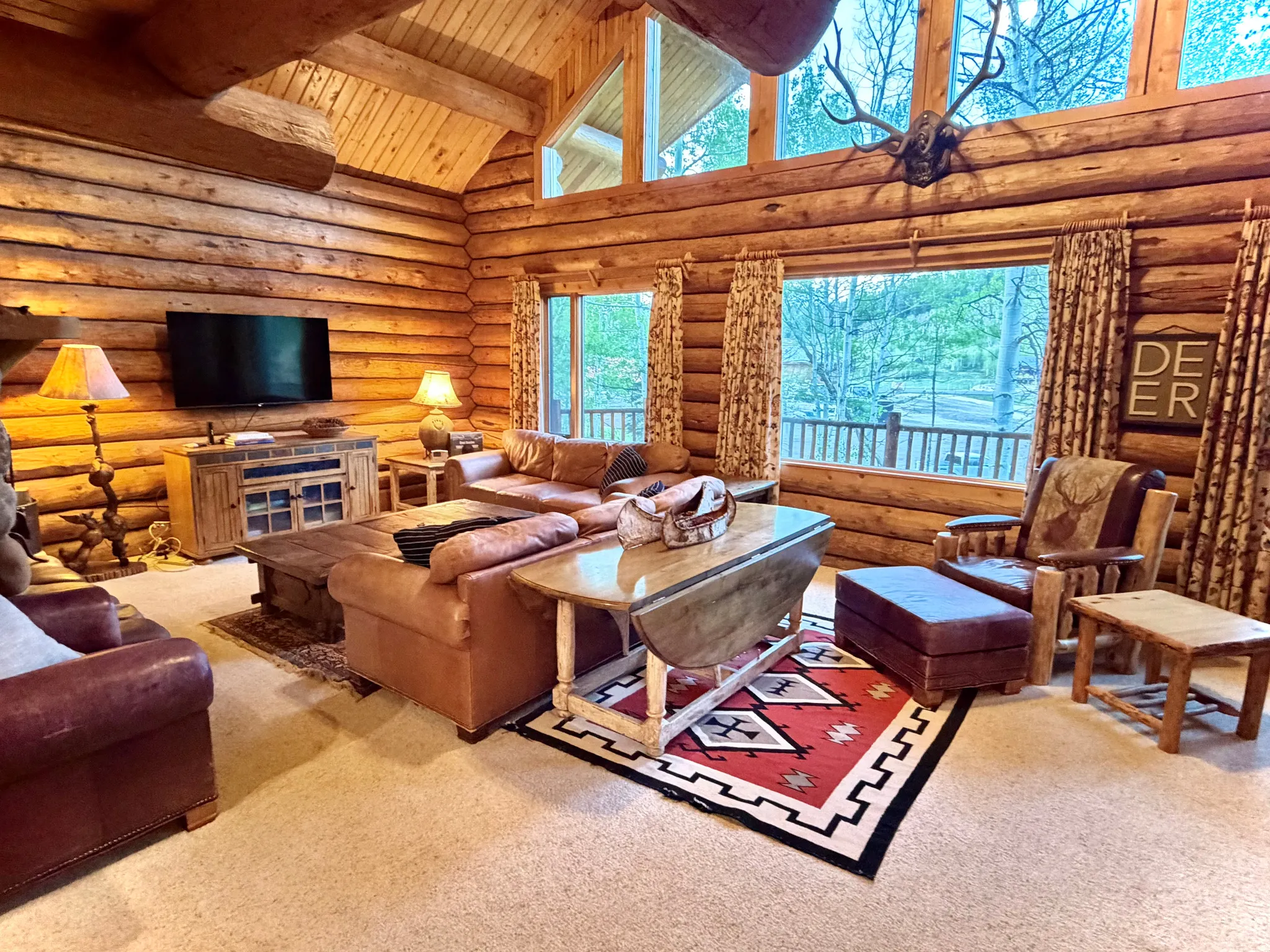 Spacious living area featuring log walls, vaulted ceilings with exposed log beams, and large windows