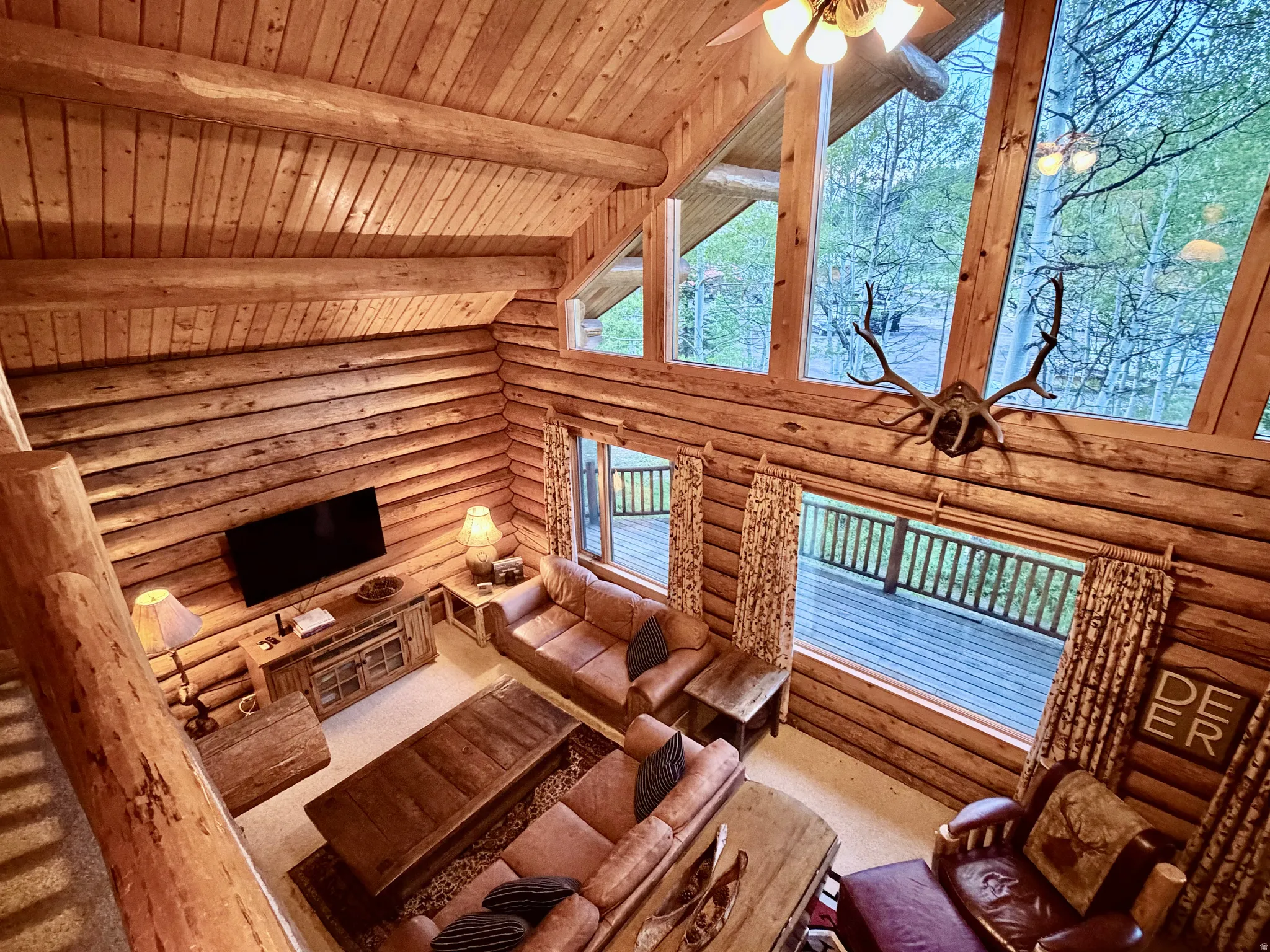 Grand great room featuring floor-to-ceiling windows, exposed log beam construction, a natural wood ceiling, and a deck accessible from the main level