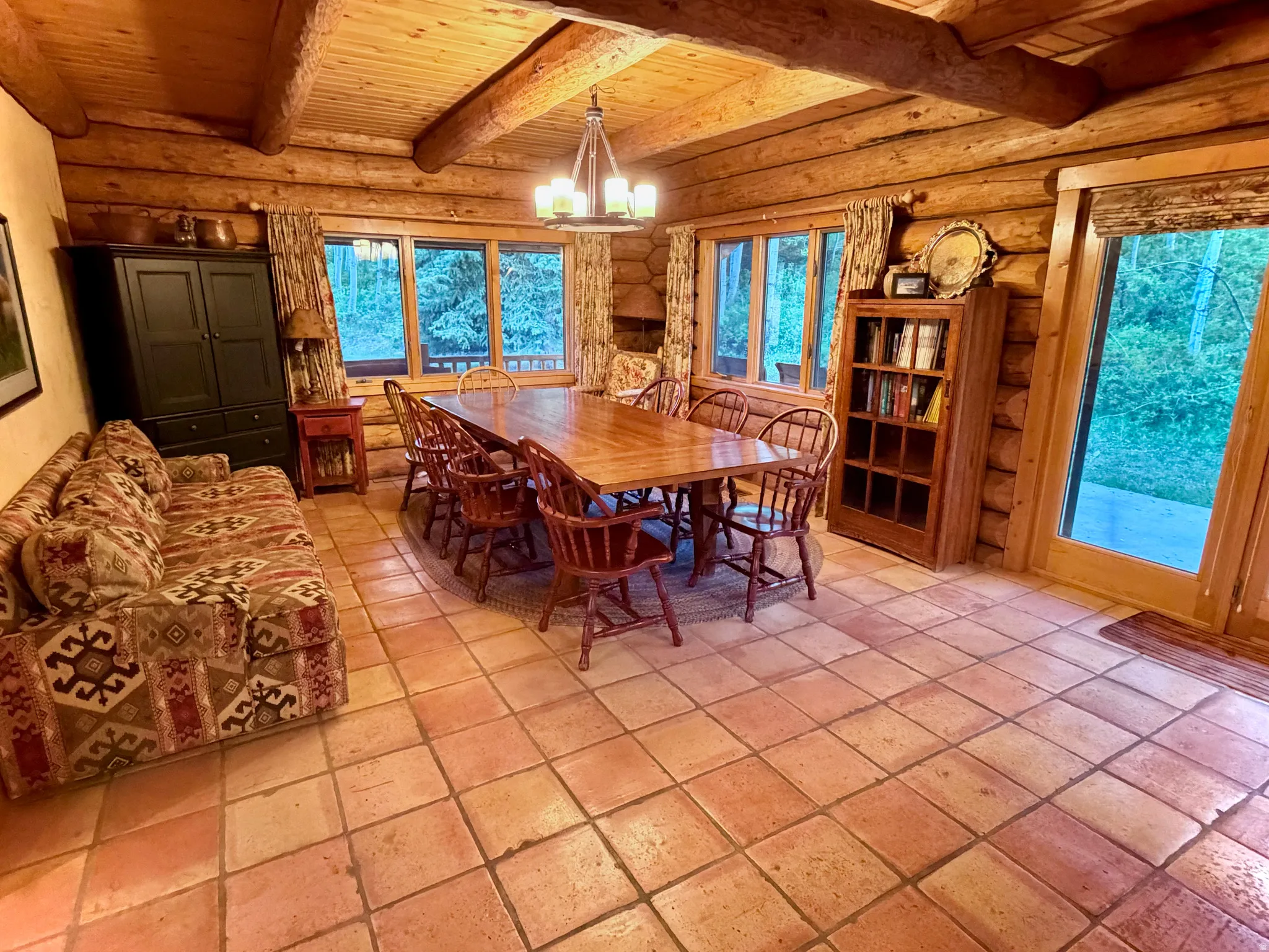 Spacious room featuring log construction, exposed beam ceiling, tile flooring, and multiple windows