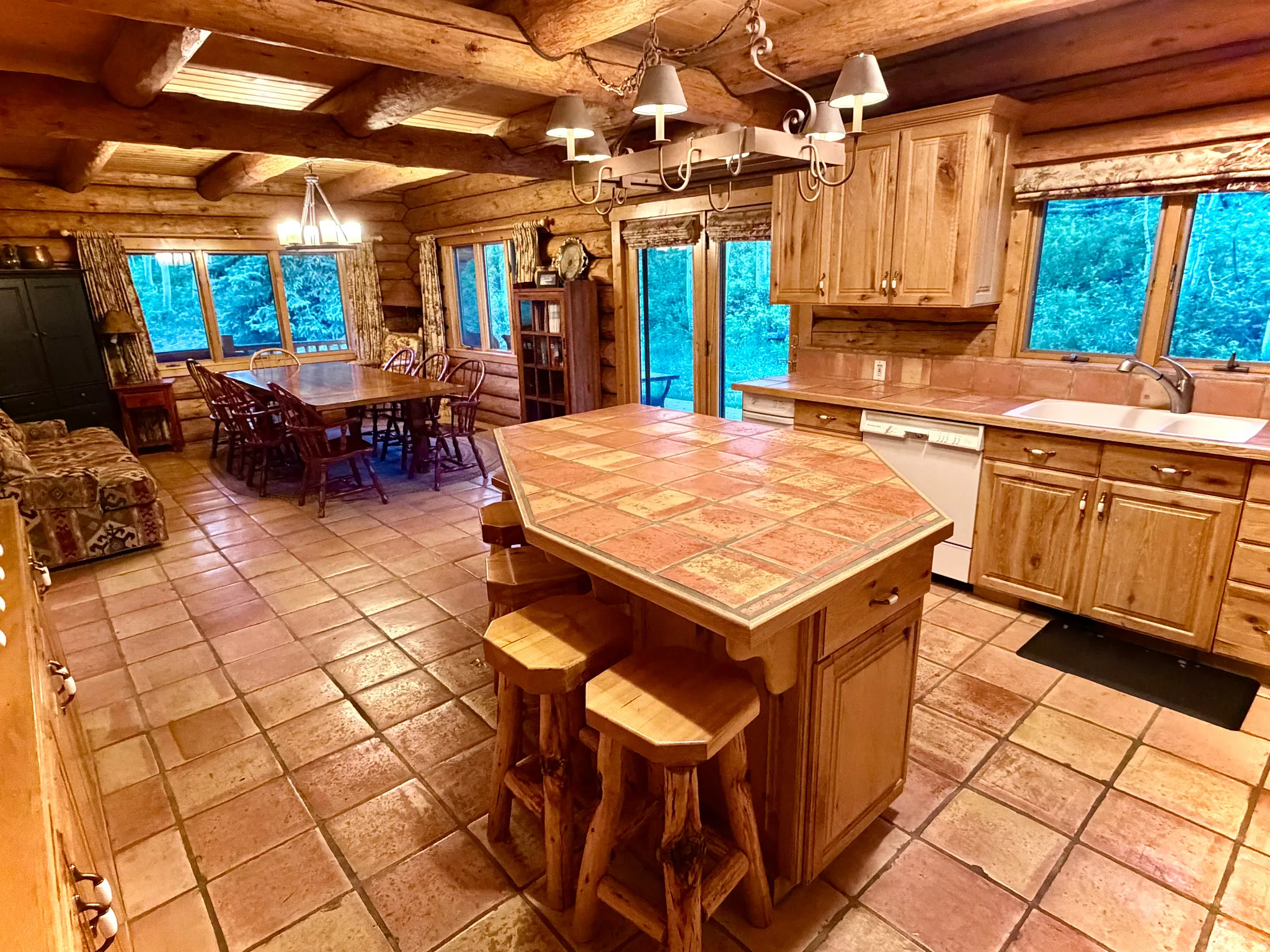 Open-concept kitchen and dining area featuring a tiled island with seating, a white basin sink, and a dishwasher