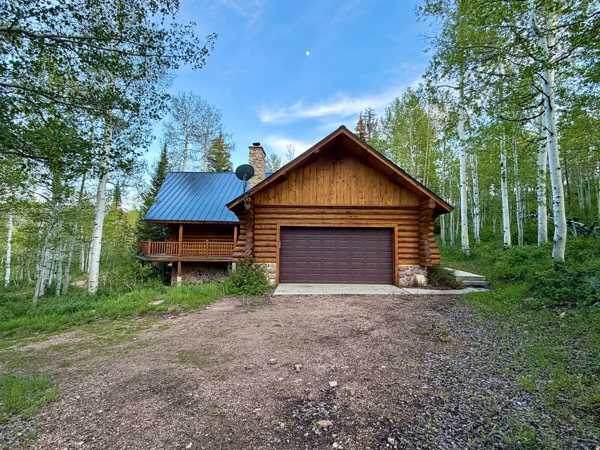 Log cabin exterior featuring a two-car garage with a brown panel door, a blue metal roof, and a stone chimney