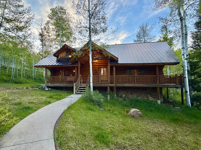Log cabin exterior featuring a dark metal roof, wrap-around porch with wood railings, and a concrete pathway