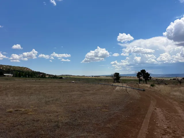 Expansive property featuring a wide-open field, distant hillsides, and a clear sky with scattered clouds