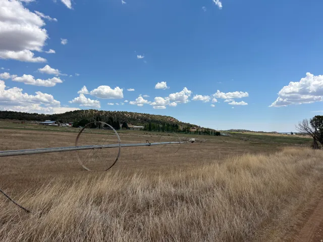 Expansive open land with natural grasses, featuring a distinct irrigation wheel and distant rolling hills