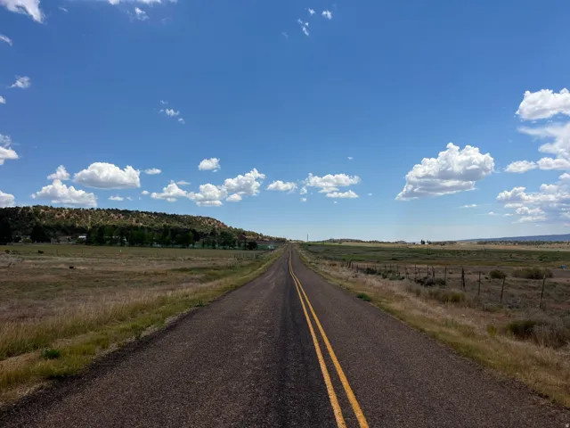 Paved road extending through open landscape with distant tree-covered hills