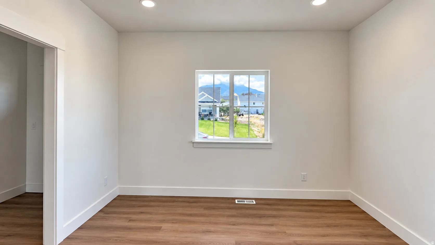 Recessed ceiling lighting, wood-finish flooring, white trim, and a window with mountain scenery