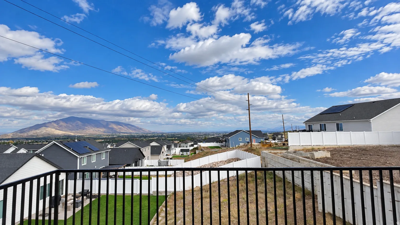 Expansive mountain backdrop with distant city elements, partially framed by a black metal railing