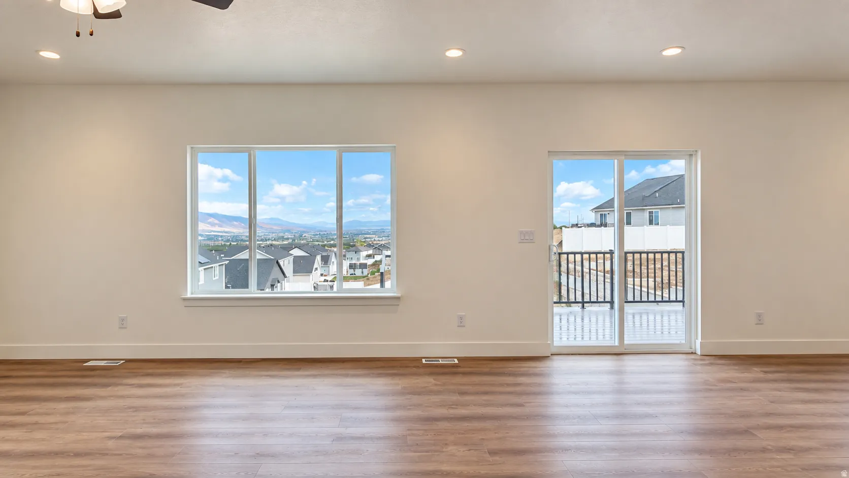 Spacious room with wood-finish flooring, recessed lighting, a large window, and a sliding glass door opening to an exterior deck with black railings