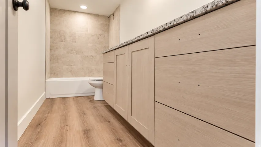 Wood-finish flooring, light-toned cabinetry, speckled countertop, tiled bathtub surround, and recessed lighting