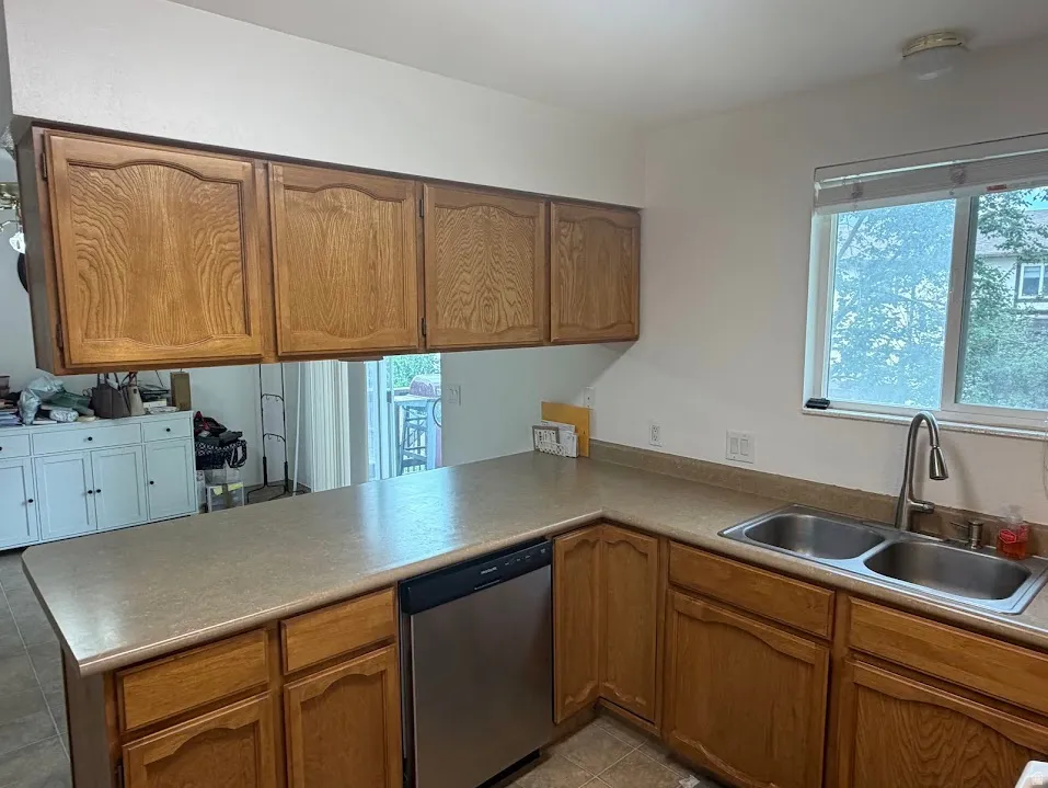 Kitchen featuring wood cabinetry, laminate countertops, a stainless steel double basin sink with a gooseneck faucet, a stainless steel dishwasher, and a window with blinds