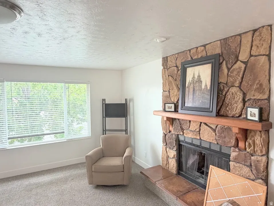 Stone-clad fireplace with a wood mantel and hearth, set against light-colored walls and grey carpeting