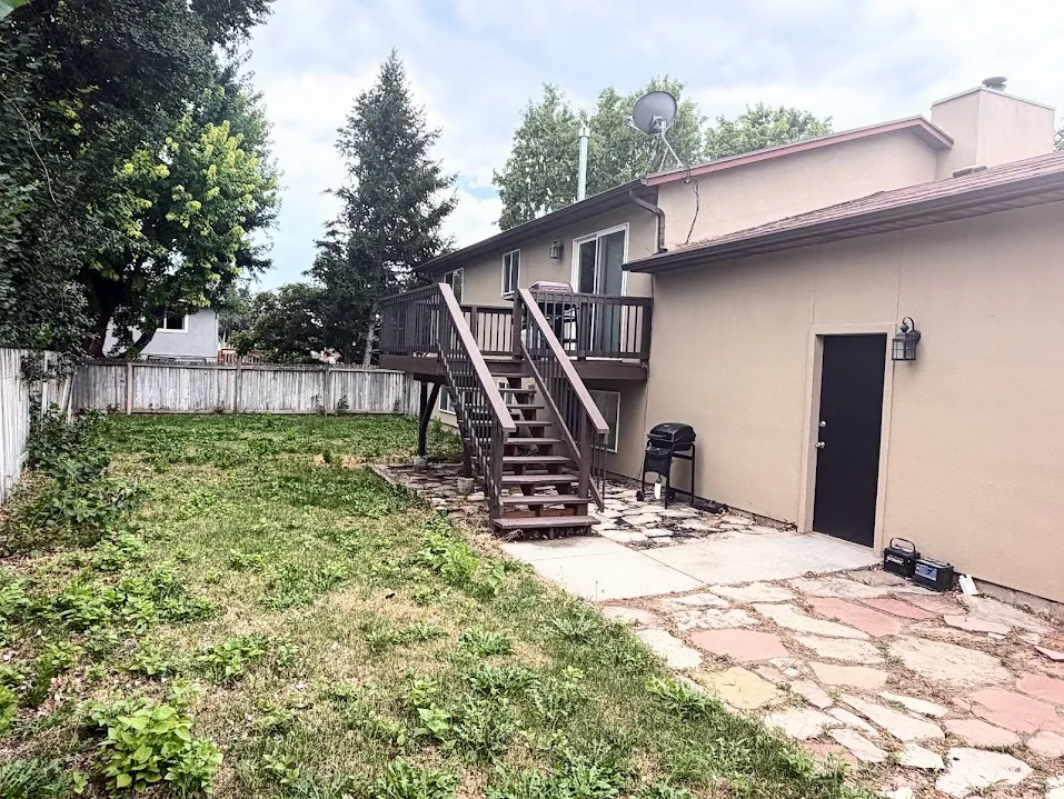Expansive backyard featuring a multi-level deck with stairs, a ground-level patio with flagstone accents, a privacy fence, and mature trees