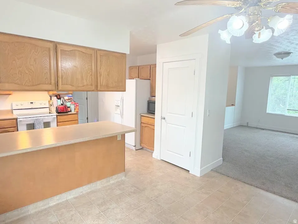 Kitchen featuring wood cabinetry, white appliances, and a breakfast bar with a light-colored countertop