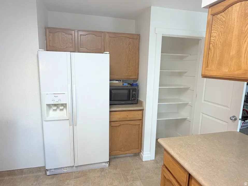 Kitchen area featuring a built-in microwave, a pantry with multiple shelves, wood-finish cabinetry, and a side-by-side refrigerator with an ice and water dispenser