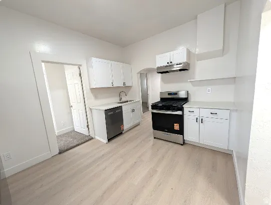 Kitchen featuring white cabinetry with dark hardware, stainless steel appliances including a dishwasher and range, wood-finish flooring, and white countertops
