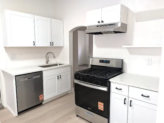 Contemporary kitchen featuring white cabinetry, light-toned countertops, stainless steel appliances, and wood-finish flooring