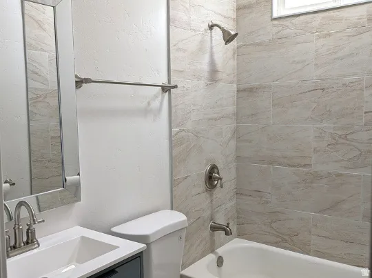 Bathroom featuring a white vanity with an integrated sink, brushed nickel hardware, and a tub-shower combination with floor-to-ceiling tile surround