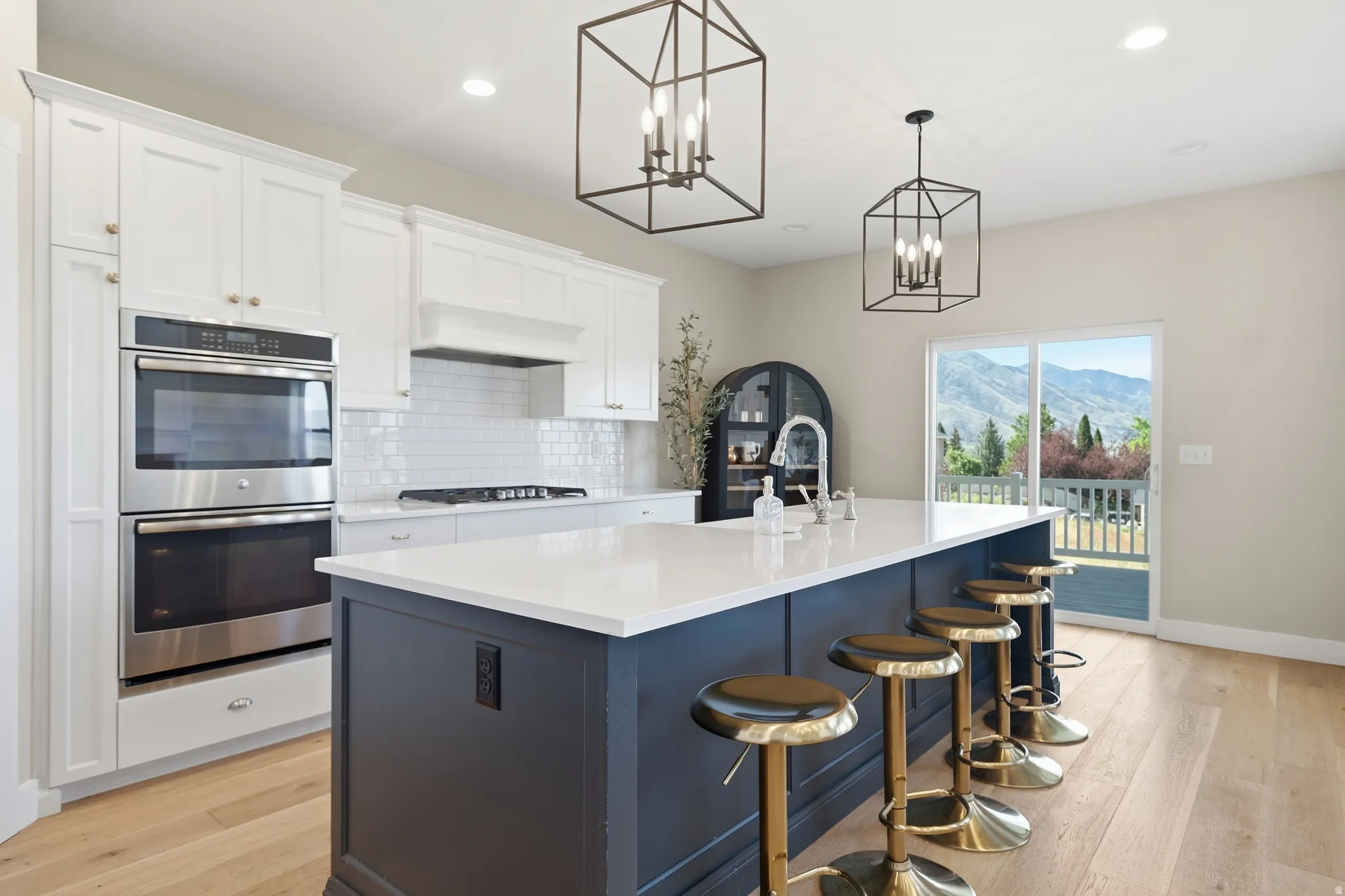 Modern kitchen featuring a large central island with seating, white shaker cabinetry, stainless steel double wall ovens, a gas range with a tile backsplash, and light wood-finish flooring