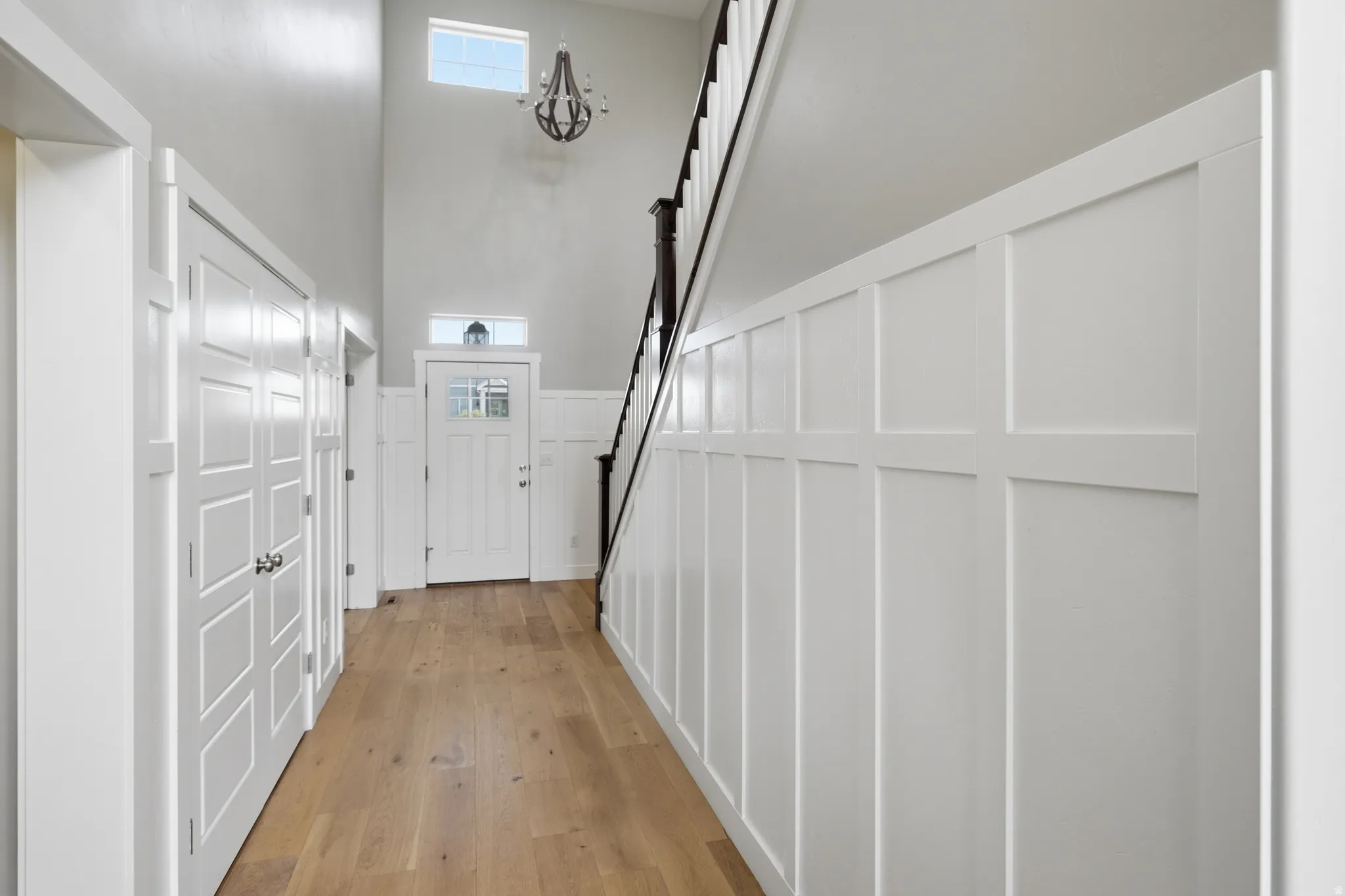 Two-story entryway featuring wood-finish flooring, white wainscoting, an accent door with glass panels, and a wood-tone chandelier
