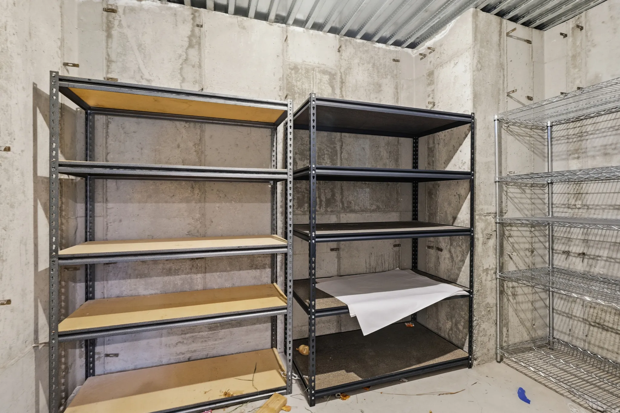 Utility area featuring concrete walls, a corrugated metal ceiling, and multiple shelving units