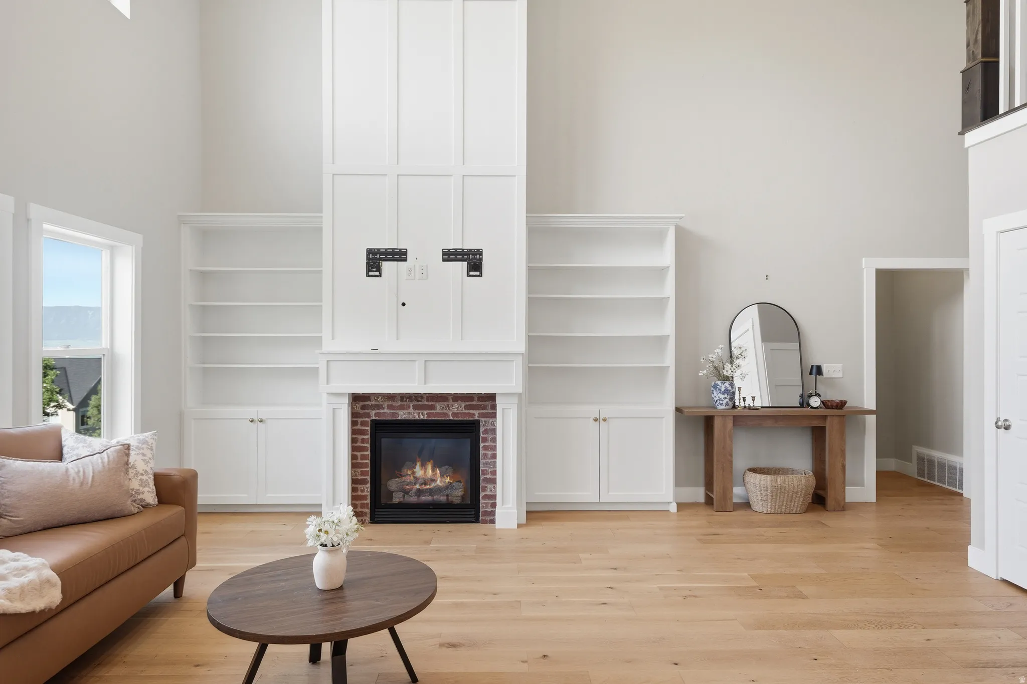 Living area featuring vaulted ceilings, a brick-surround fireplace with a white mantel, and built-in white cabinetry with open shelving