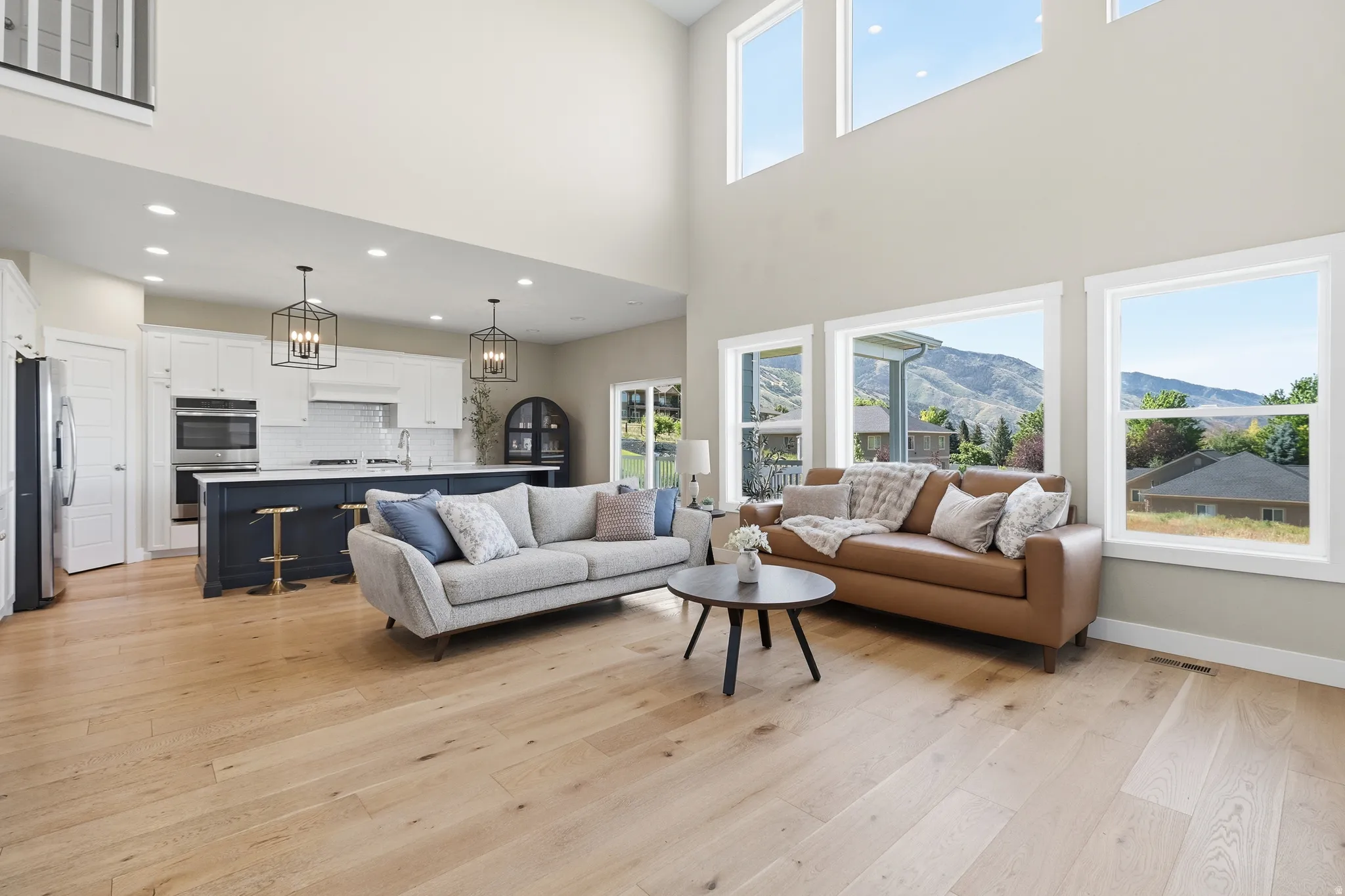 Open-concept great room featuring expansive windows, wood-finish flooring, a two-story ceiling, and a large kitchen island with pendant lighting