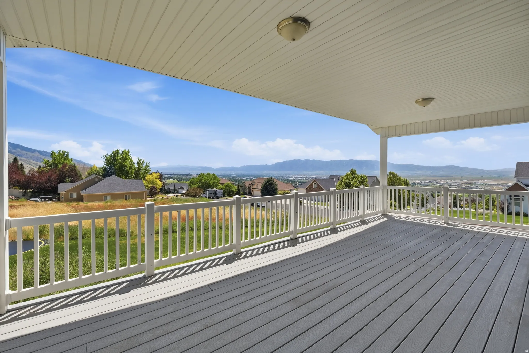Expansive covered deck featuring composite decking and white railing, offering elevated neighborhood and mountain scenery