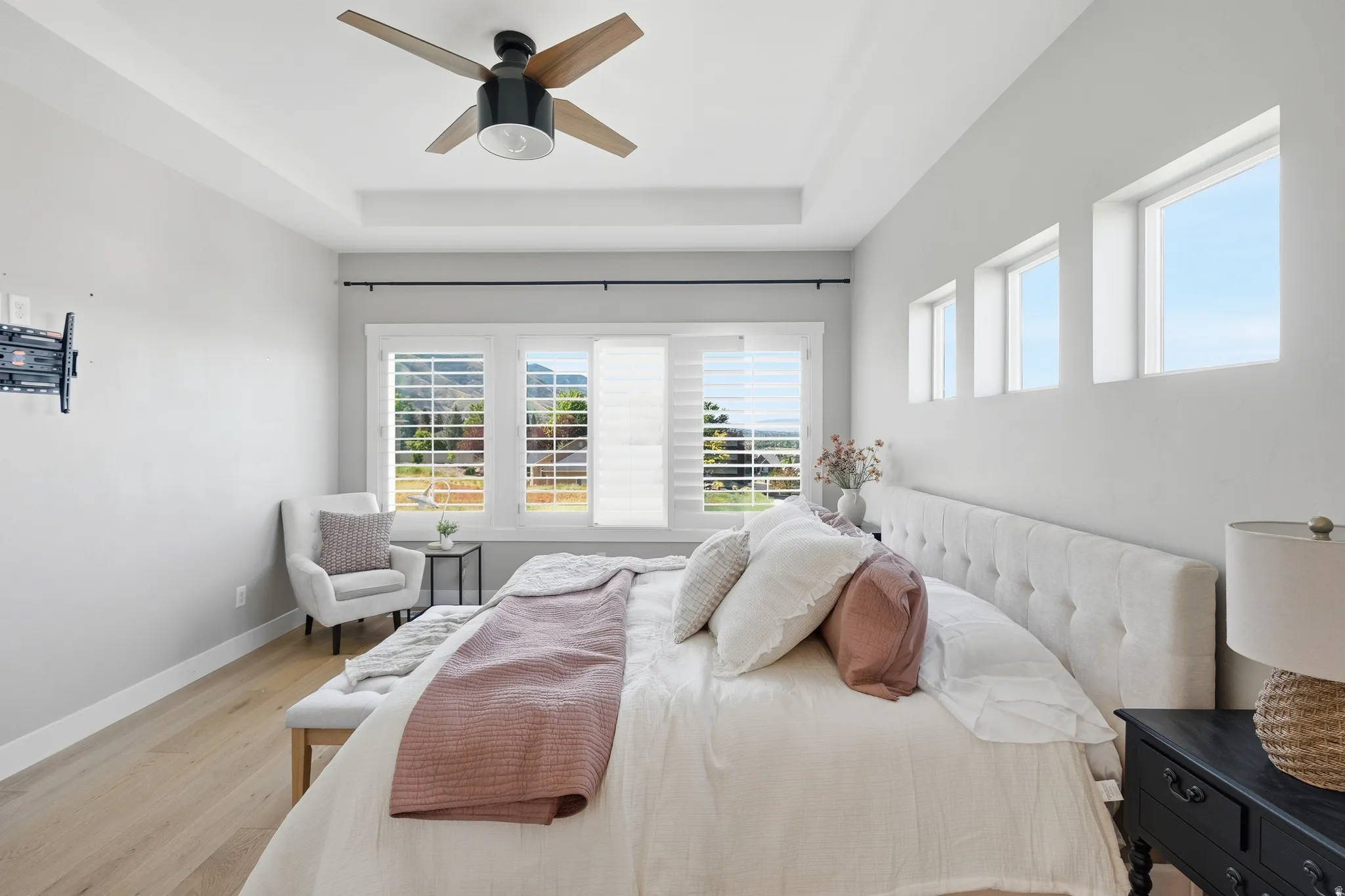 Spacious bedroom featuring light wood-finish flooring, a tray ceiling, and a contemporary ceiling fan