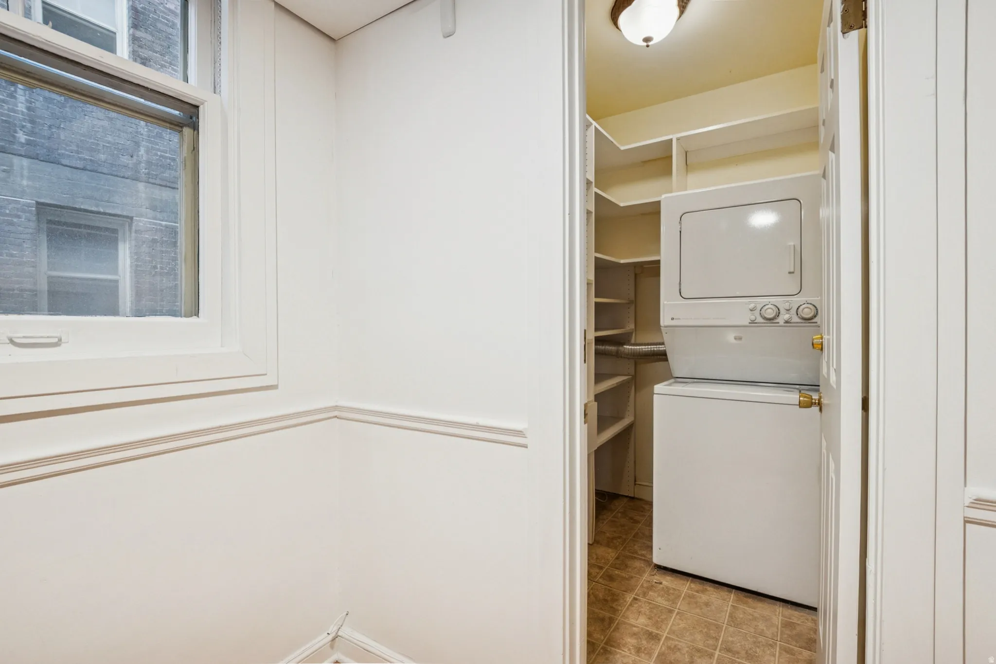 Dedicated laundry area with a stacked washer and dryer, complemented by built-in shelving and tile flooring