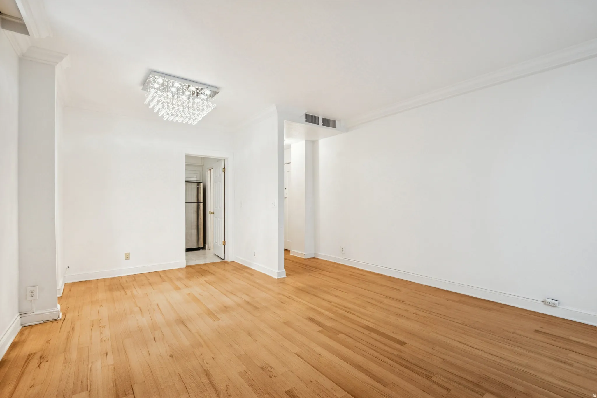 Open-concept living space featuring wood-finish flooring, white painted walls, a decorative ceiling light fixture, and crown molding
