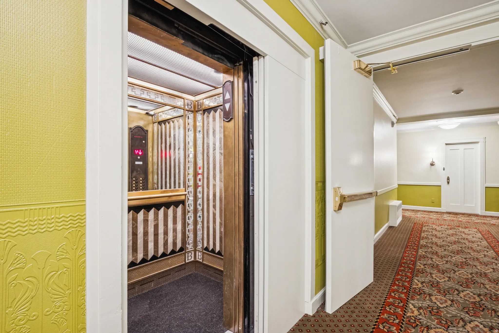 Ornate elevator cab featuring a patterned bronze interior, mirrored panels, and carpeted floor