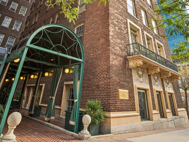 Brick facade building featuring a green metal entryway canopy, decorative balcony with wrought iron railing, and patterned architectural accents