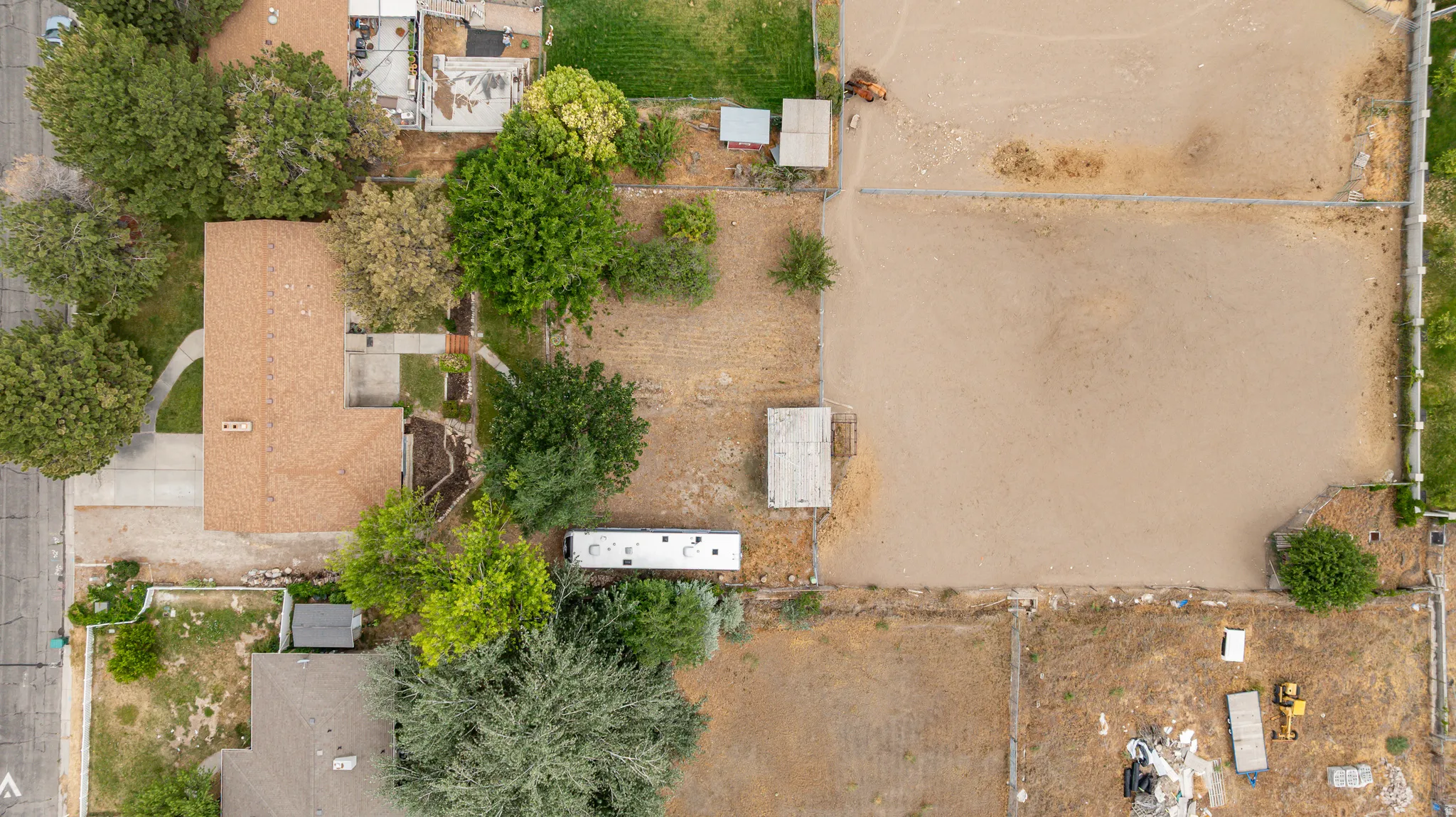Aerial view showcasing a residential property with a brown-shingled roof, a paved driveway, and mature trees