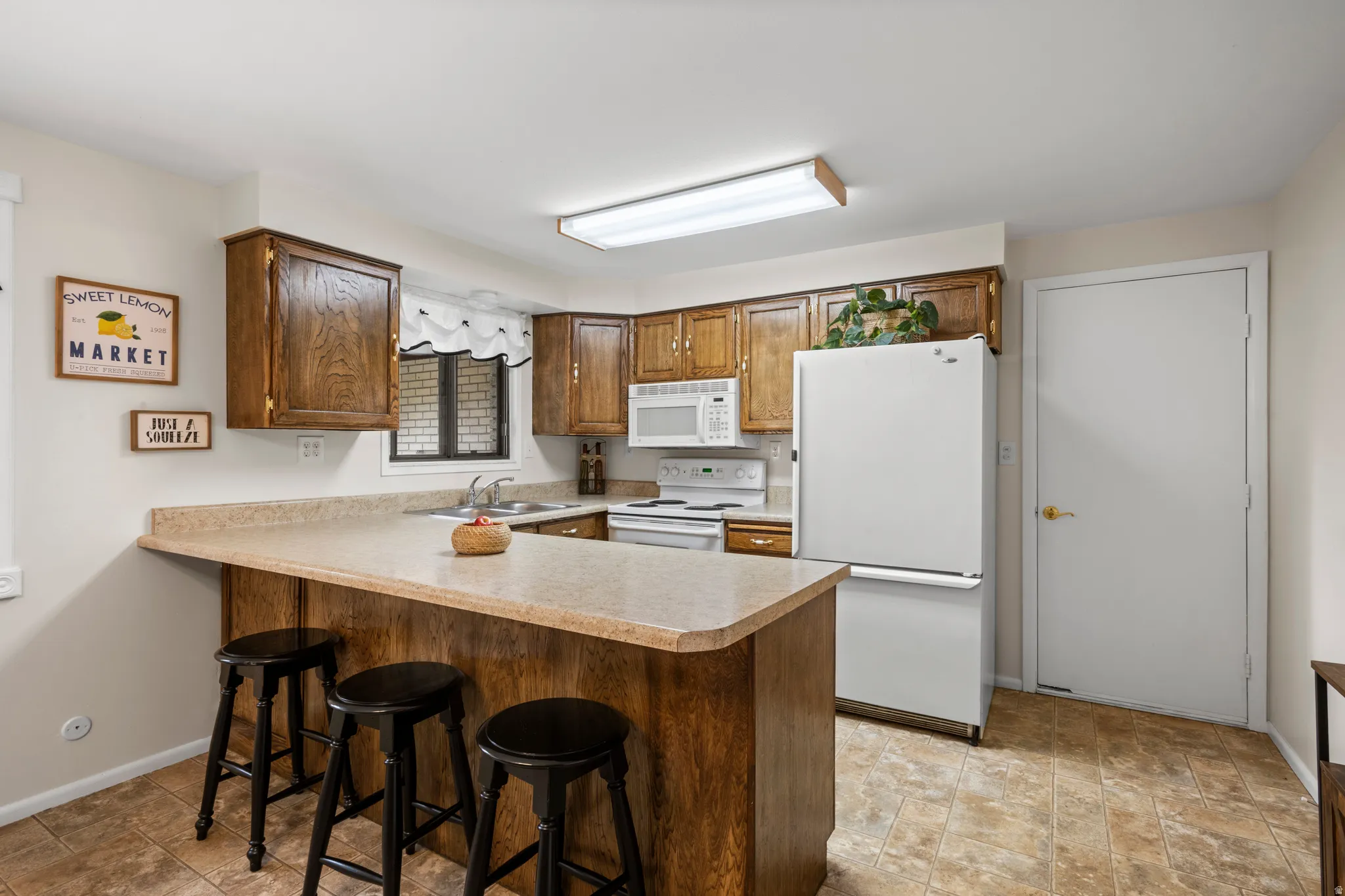 Kitchen featuring wood cabinetry, laminate countertops, a built-in microwave, white refrigerator, and tile flooring