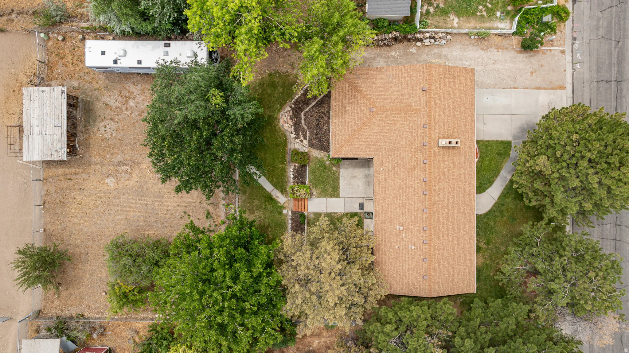 Expansive lot featuring a single-story residence with a brown shingle roof, concrete driveway, and mature landscaping