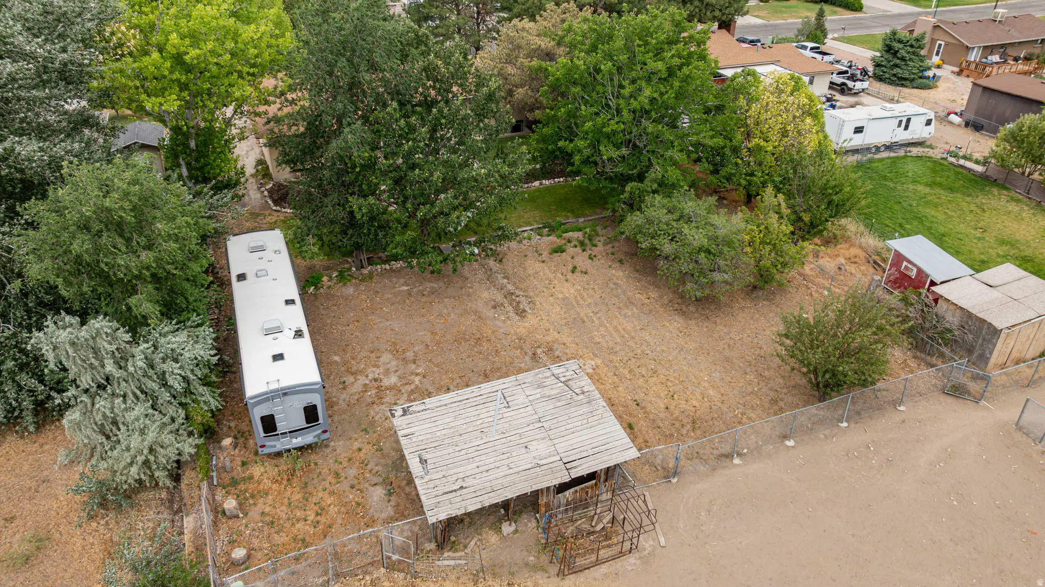 Expansive parcel featuring a large open area, mature trees, and existing outbuildings and covered structure