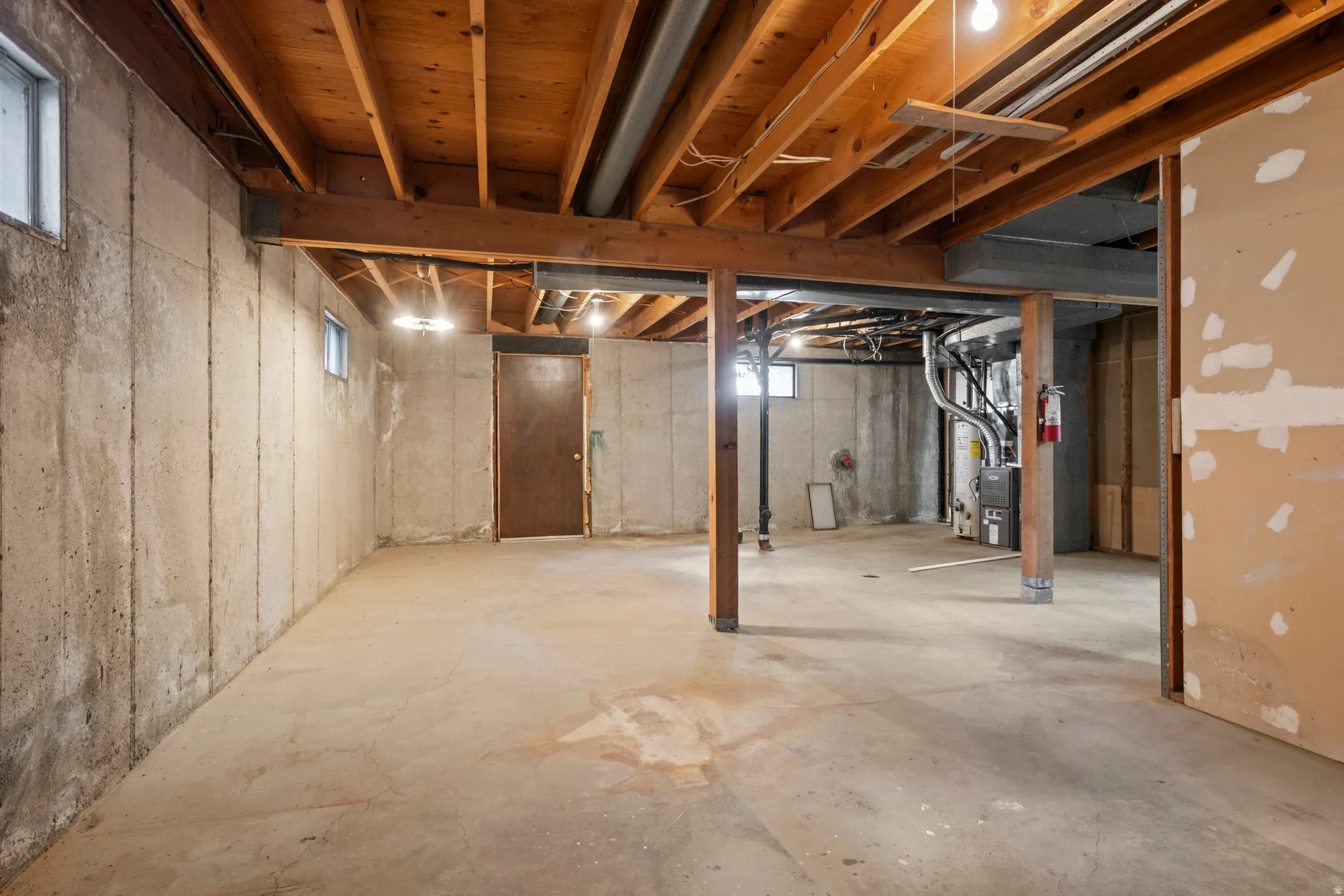 Unfinished basement featuring concrete walls and flooring, exposed wood ceiling joists, wood support beams, and multiple windows