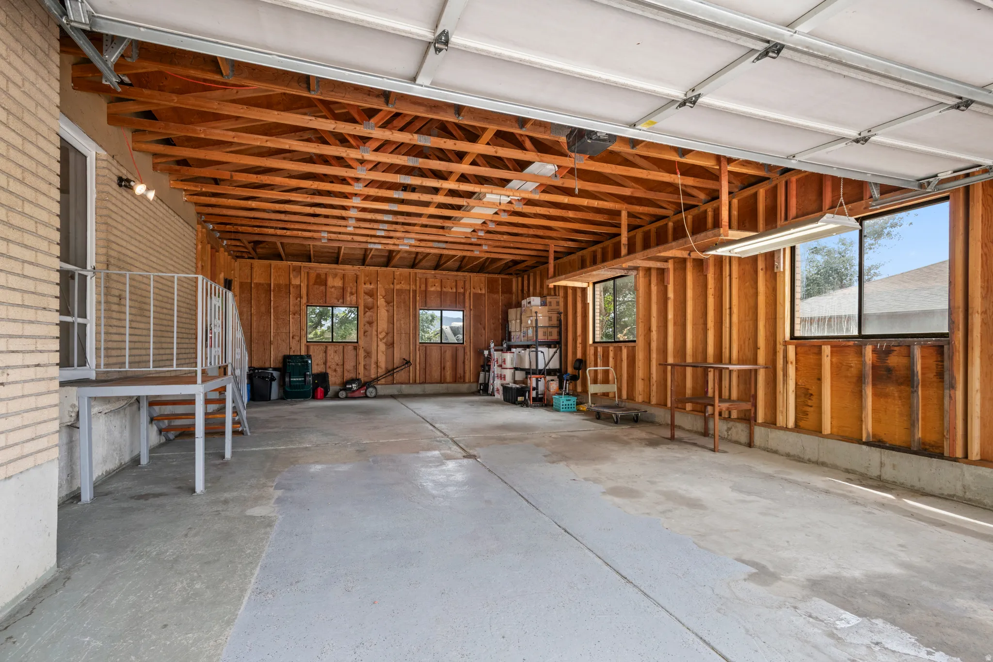 Spacious garage featuring a large concrete floor, exposed wood ceiling beams, and multiple windows