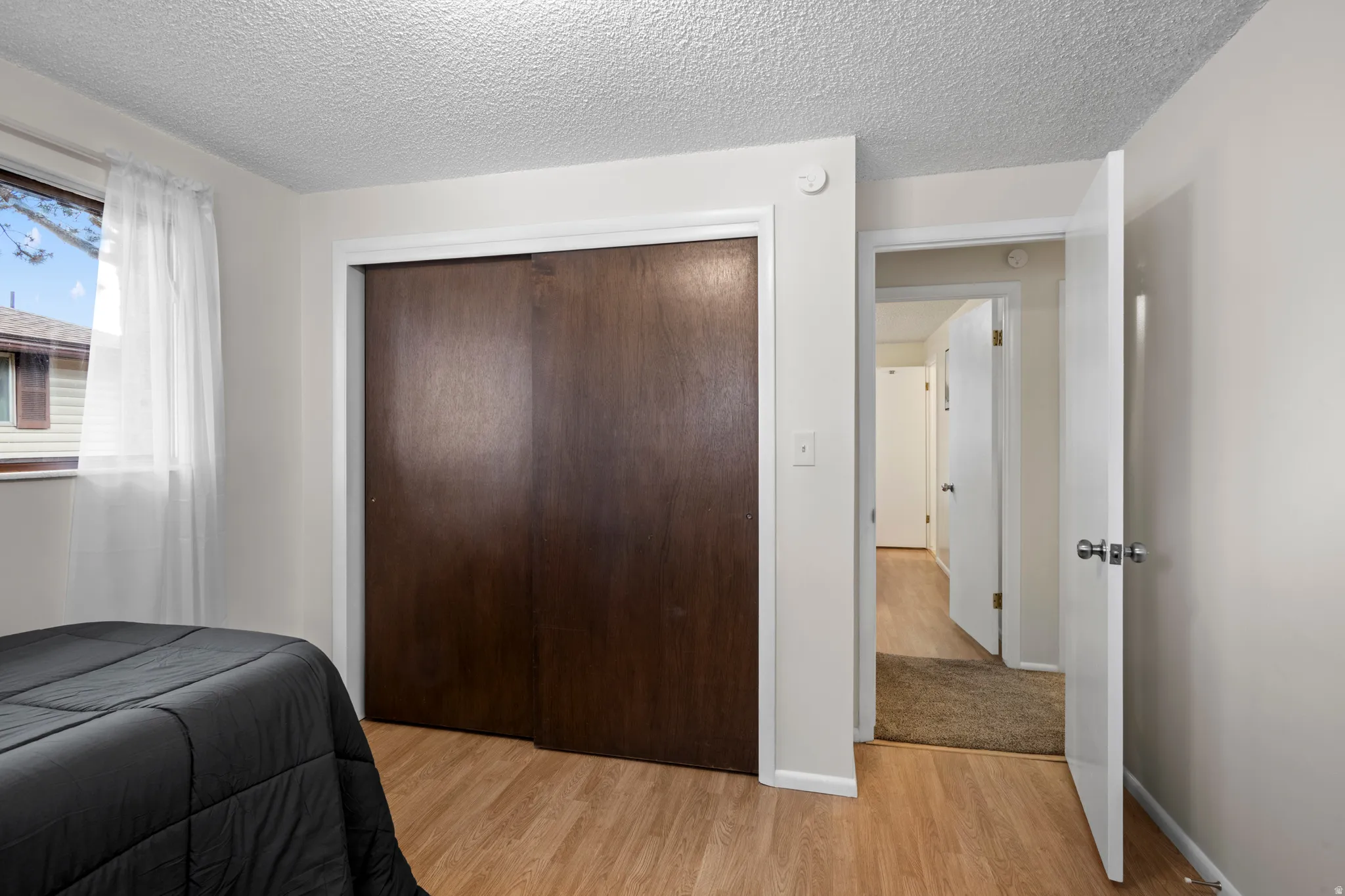 Wood-finish flooring throughout, featuring a window with white trim, a built-in closet with dark wood-finish sliding doors, and a white interior door