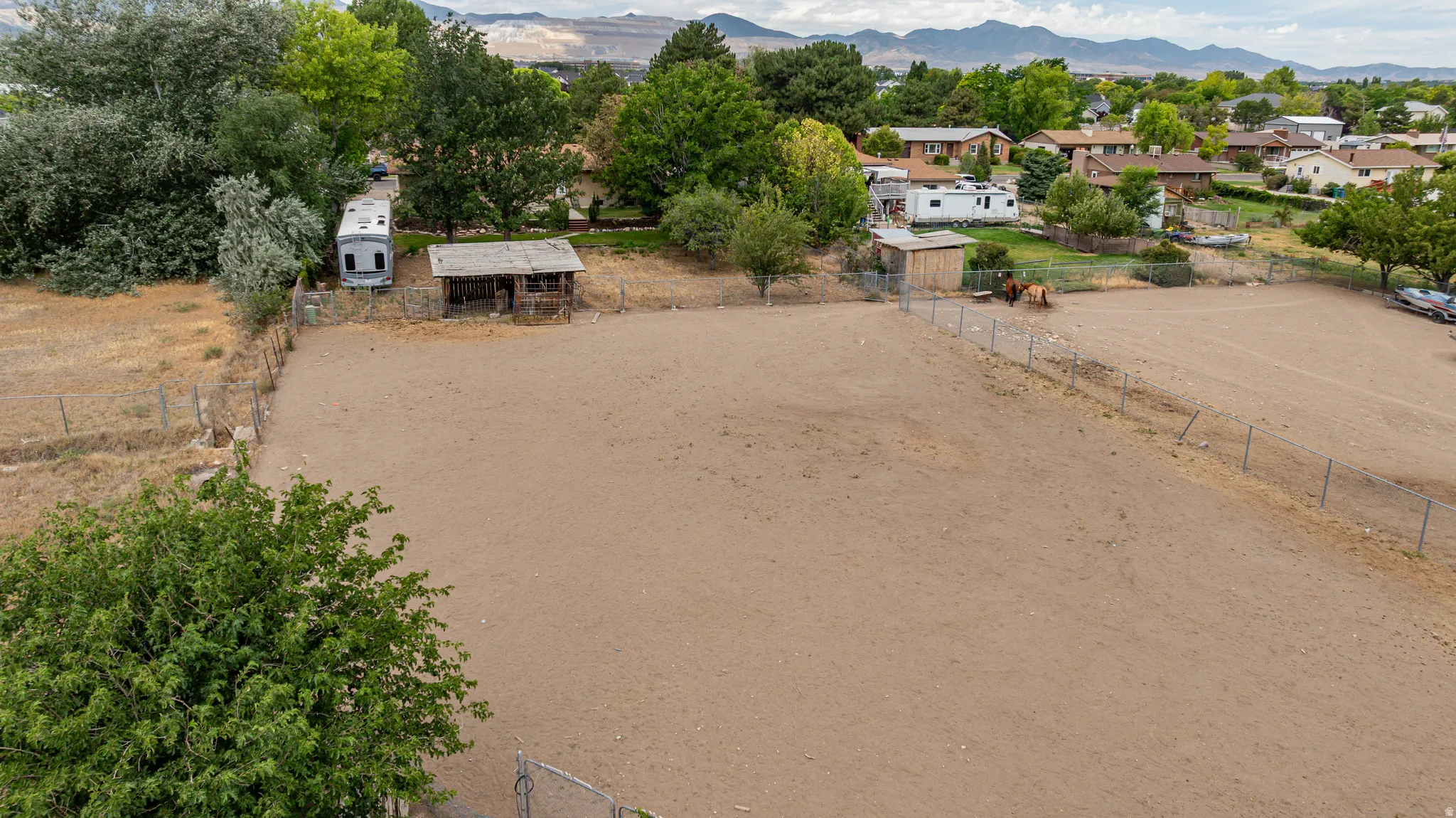 Expansive open lot featuring a perimeter fence, mature trees, and mountainous terrain in the background